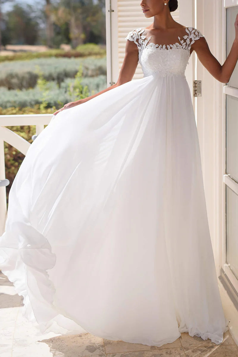 Model wearing an A-line beach wedding dress with short sleeves and lace appliques, standing outdoors.