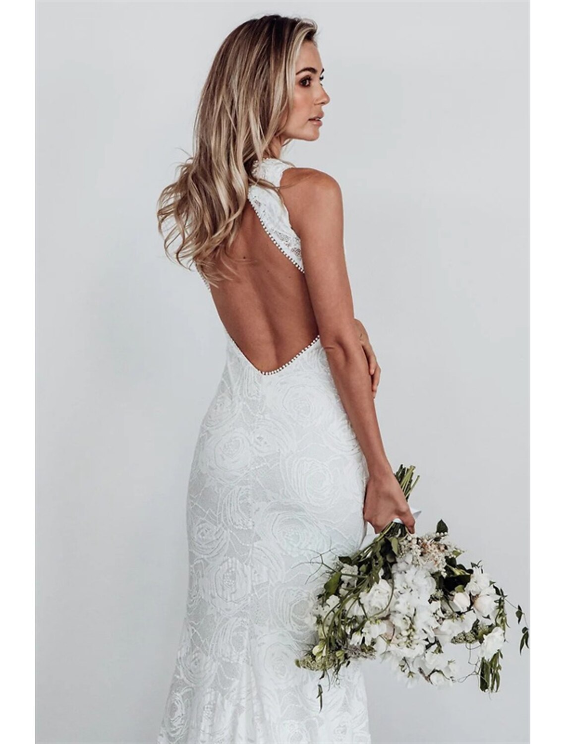 Woman wearing a white boho lace mermaid wedding dress with a halter neckline and open back.