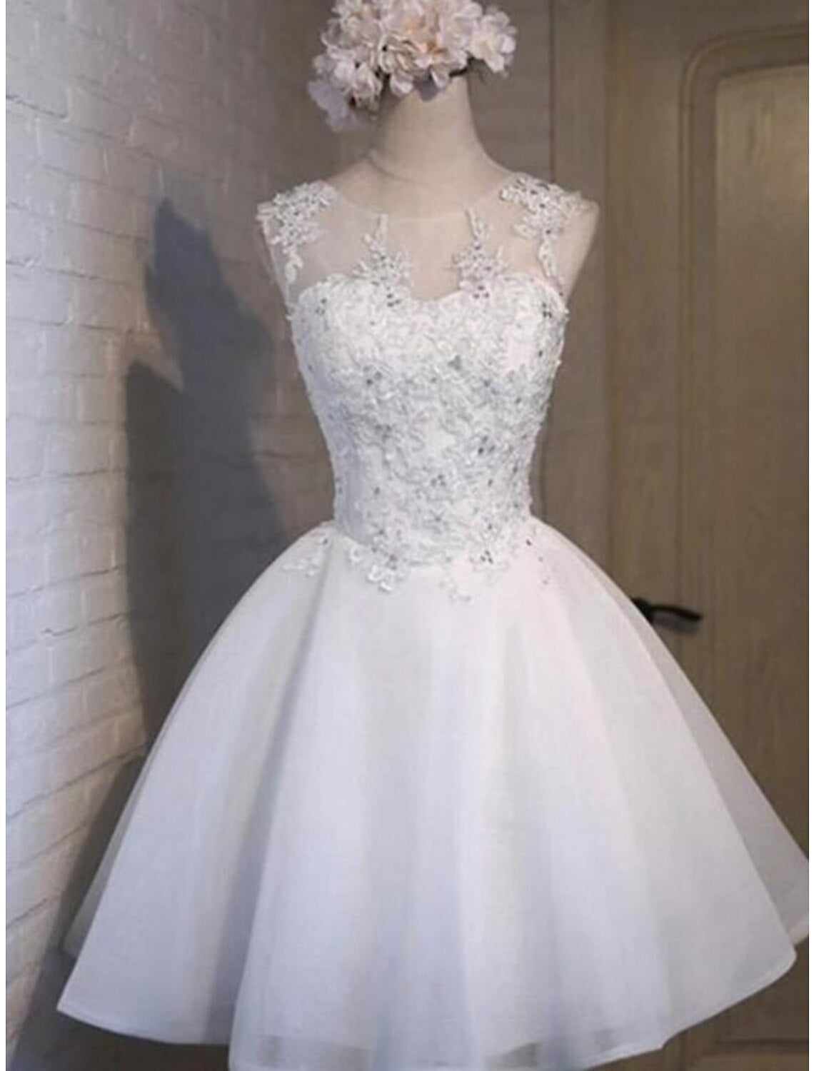 Model wearing a blush pink A-line short homecoming dress with floral appliques and jewel neck.