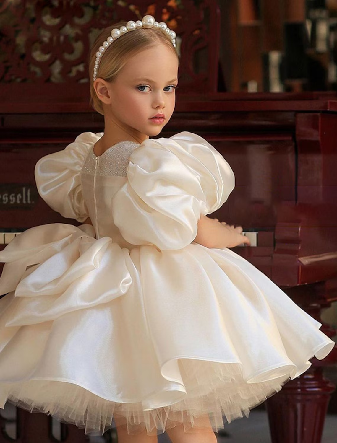 Young girl in white A-line puff sleeve dress with large back bow.