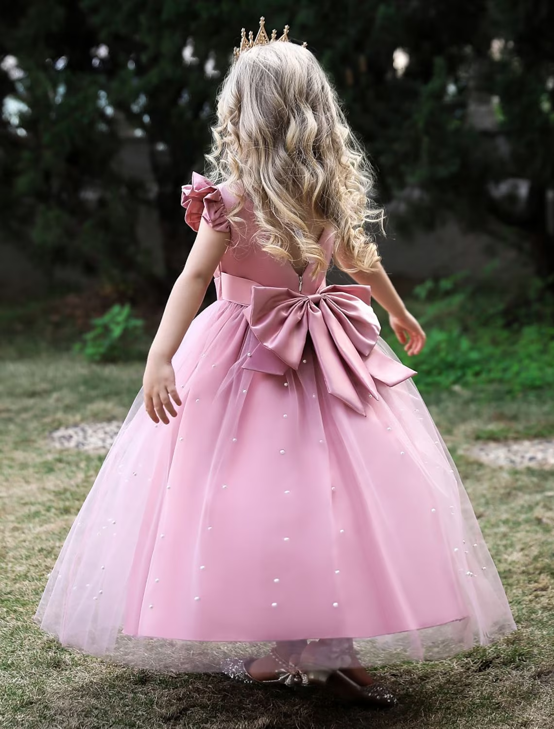 Young girl wearing a dusty rose sleeveless princess tulle maxi dress with a bow.