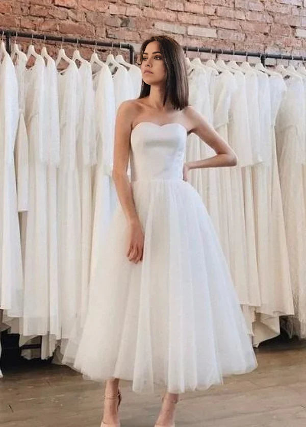Model wearing an A-line backless strapless tea-length tulle wedding dress.