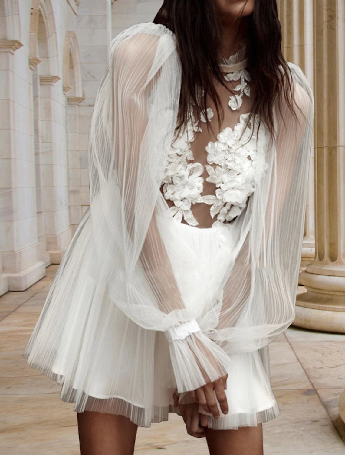 Close-up of satin fabric, pleats, and appliques on white mini dress.