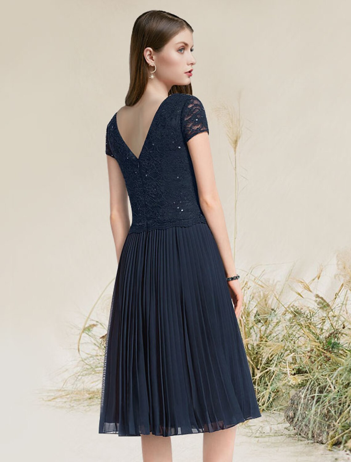 Back view of a woman in a pleated tea length A-line cocktail dress.