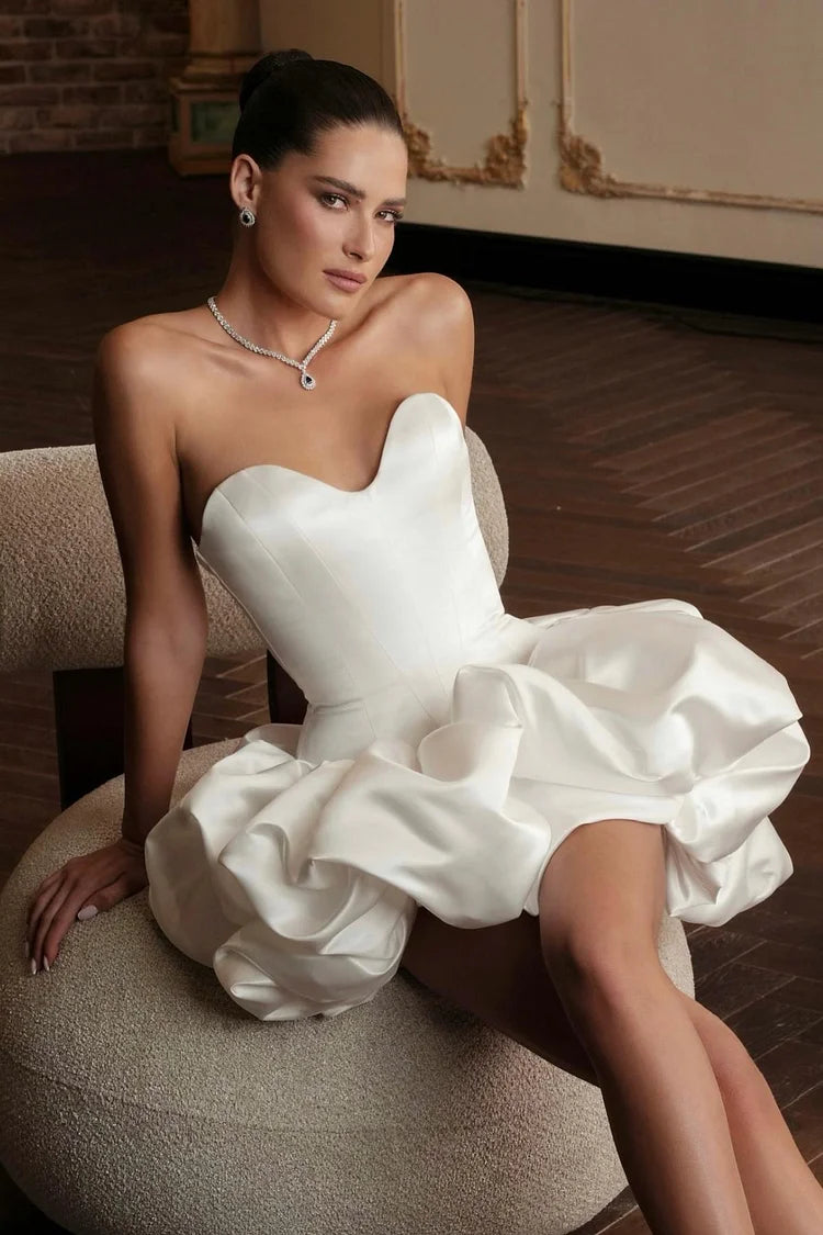 Model wearing a white satin strapless short prom dress with ruffles.
