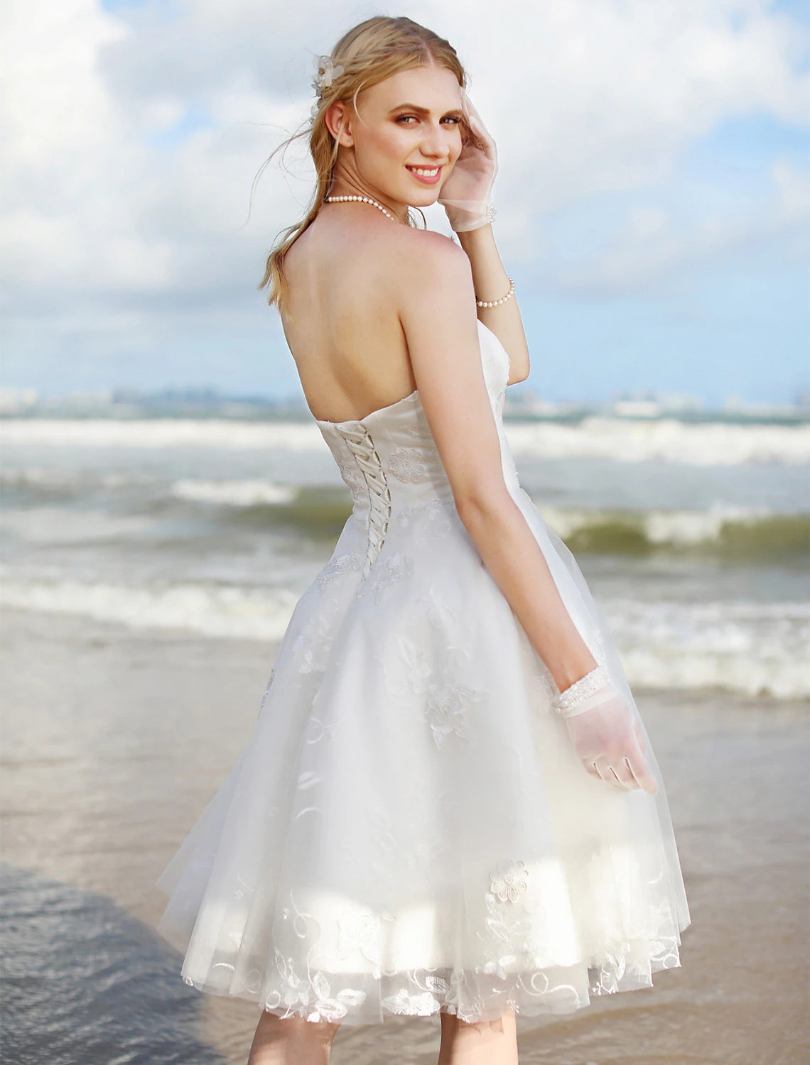 Back view of a knee-length lace bridal gown with a flowing skirt.