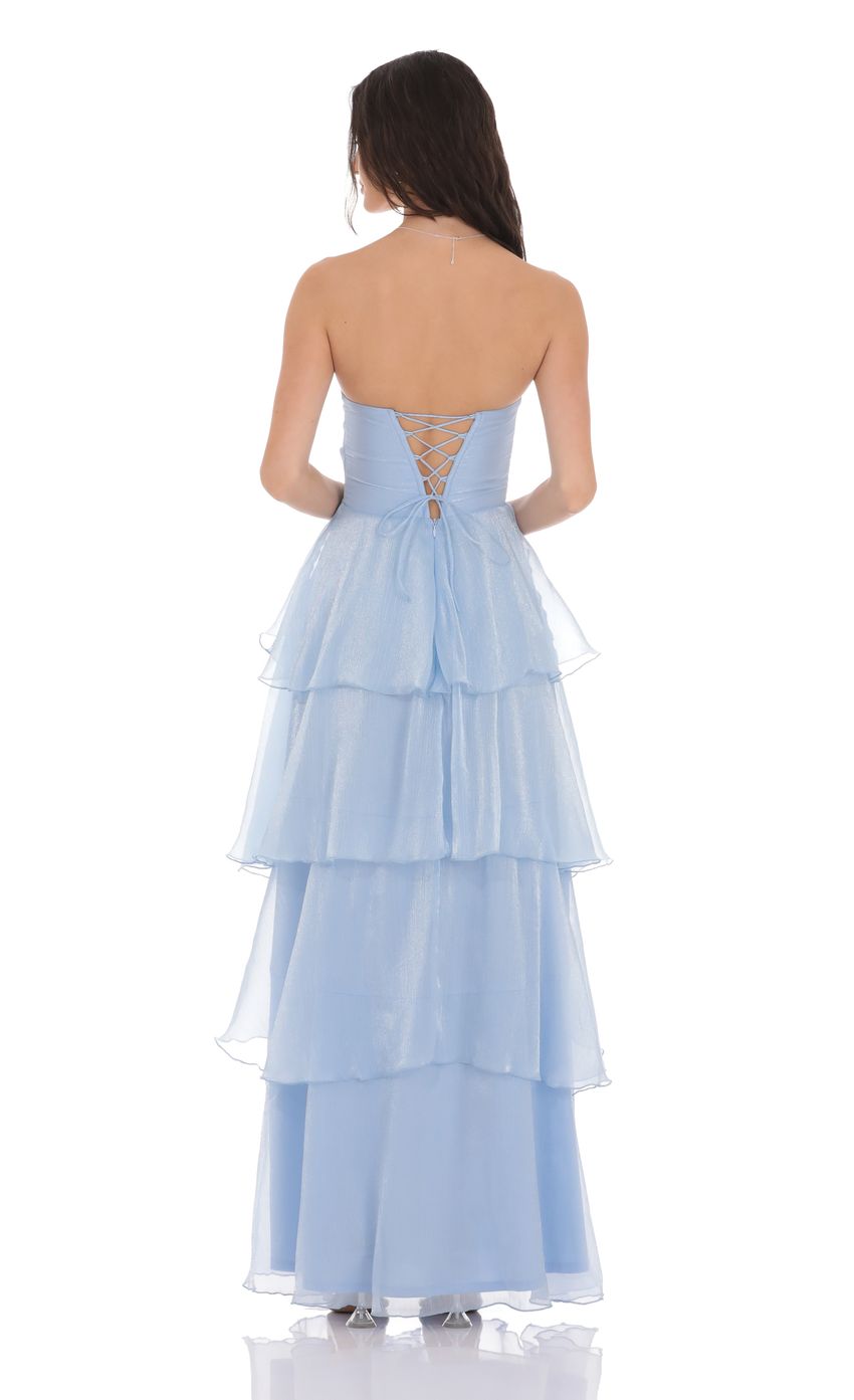 Model in a sky blue strapless maxi dress with cascading ruffles, side view.