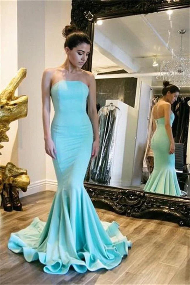 Woman wearing a navy blue mermaid strapless satin long prom dress.