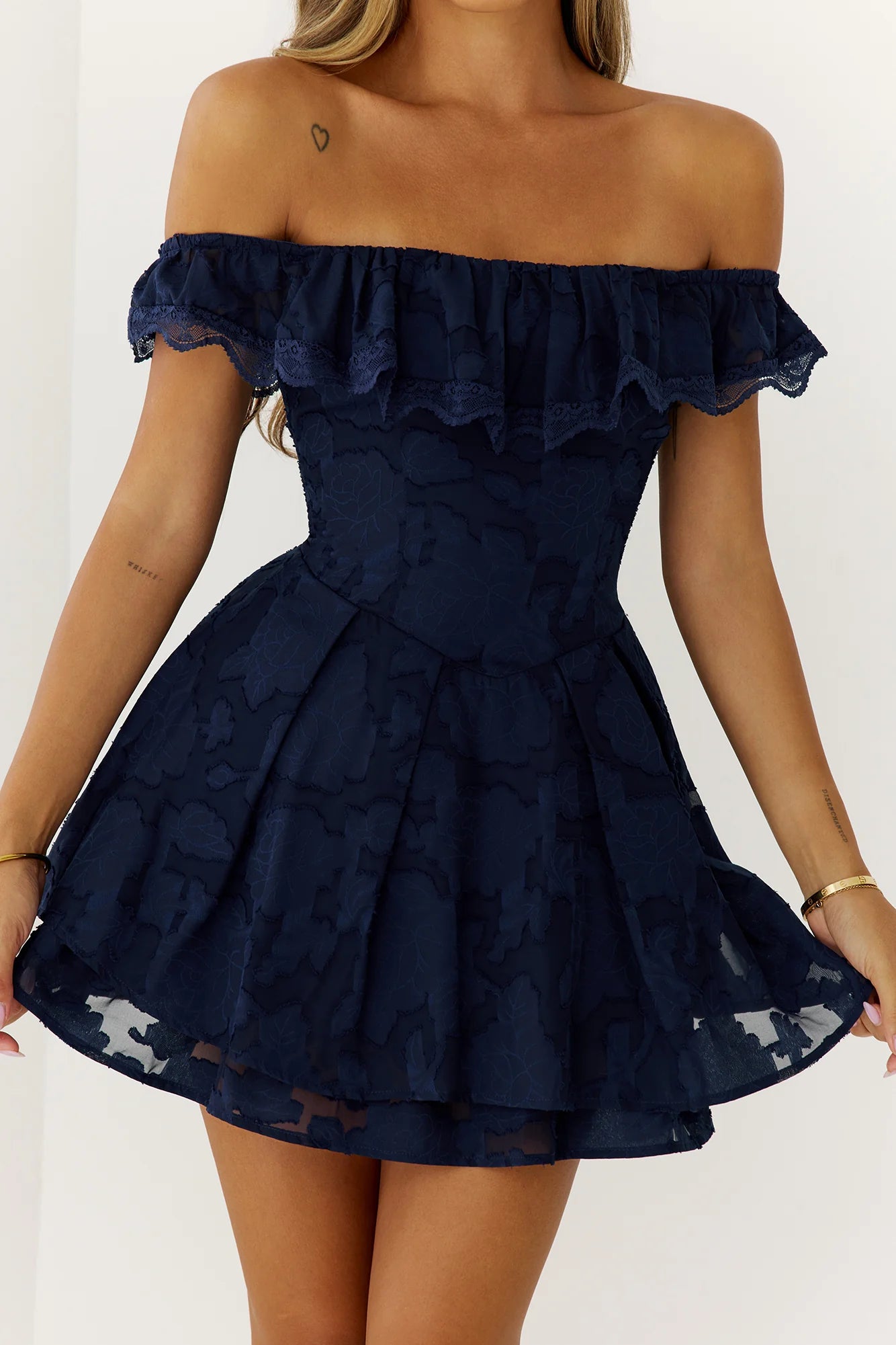 Model wearing a navy blue lace off-shoulder homecoming dress with ruffle trim and flared mini skirt.
