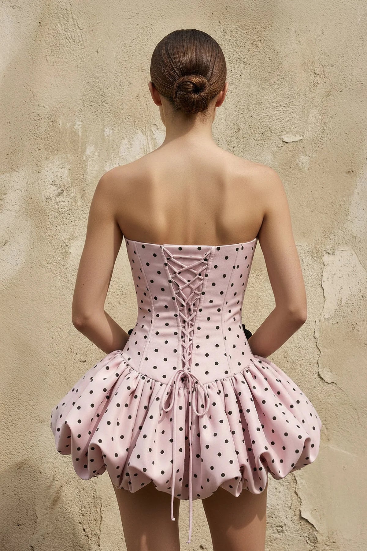 Back view of pink polka dot mini dress showing lace-up corset detail.