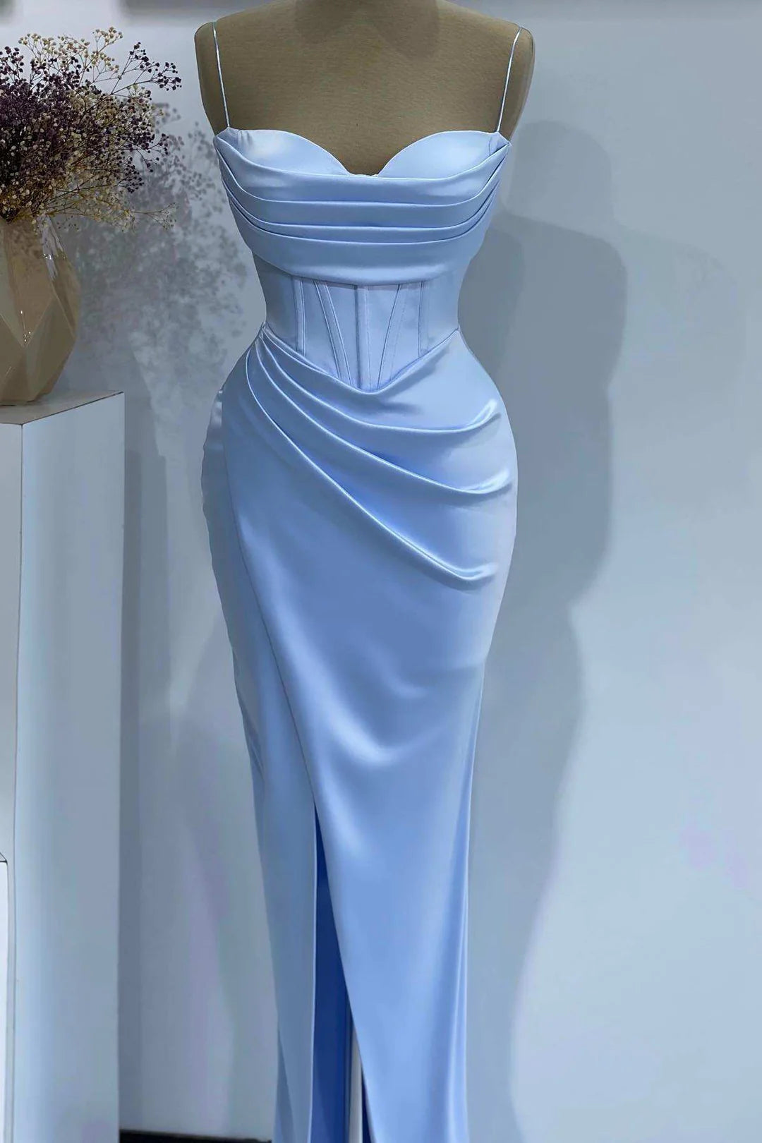 Model wearing a light blue satin sheath formal dress with spaghetti straps and a side slit.