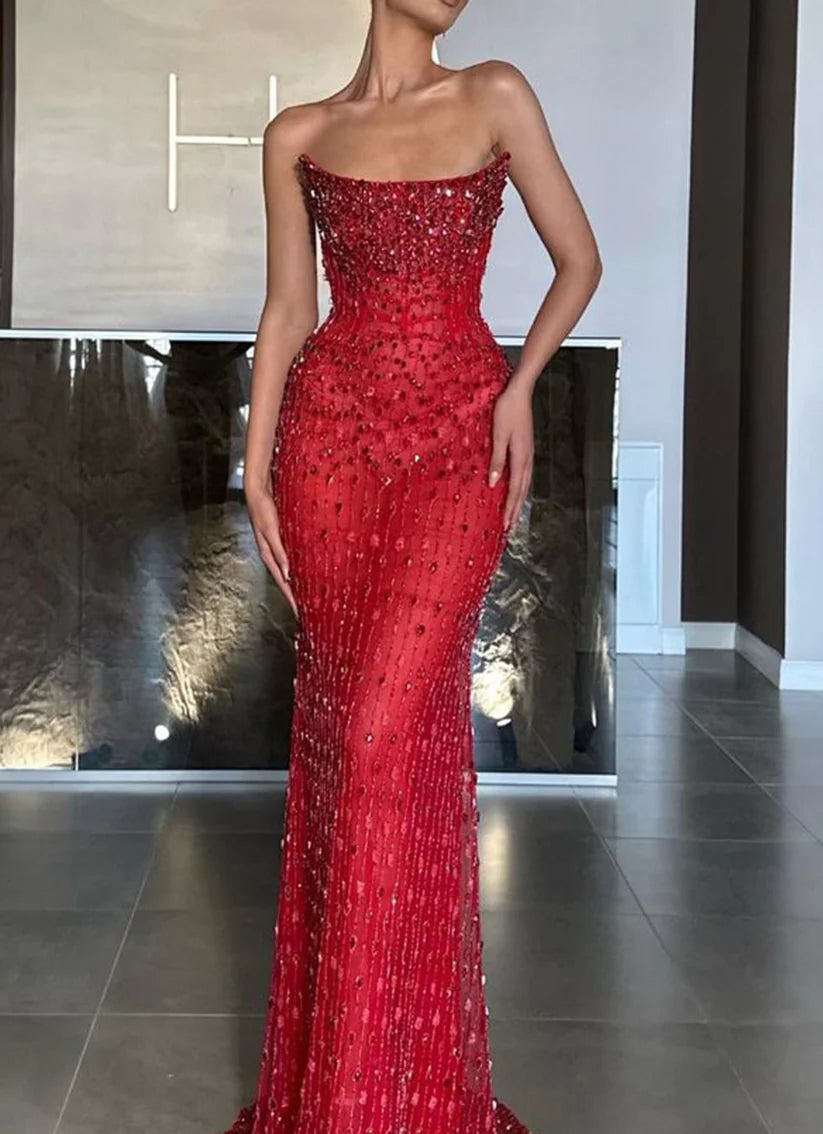 Woman wearing a dazzling sequined and beaded mermaid prom dress with a boat neck and train.