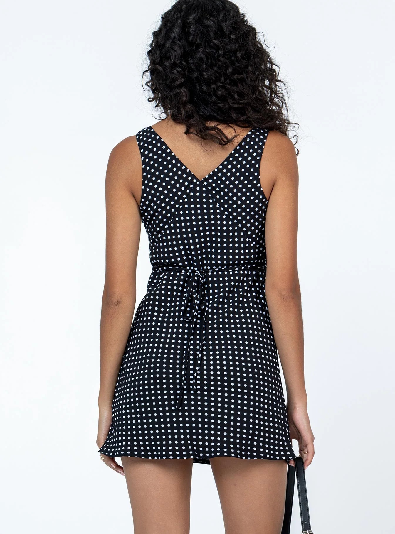 Back view of a model in a black and white polka dot mini dress, highlighting the tie back detail.