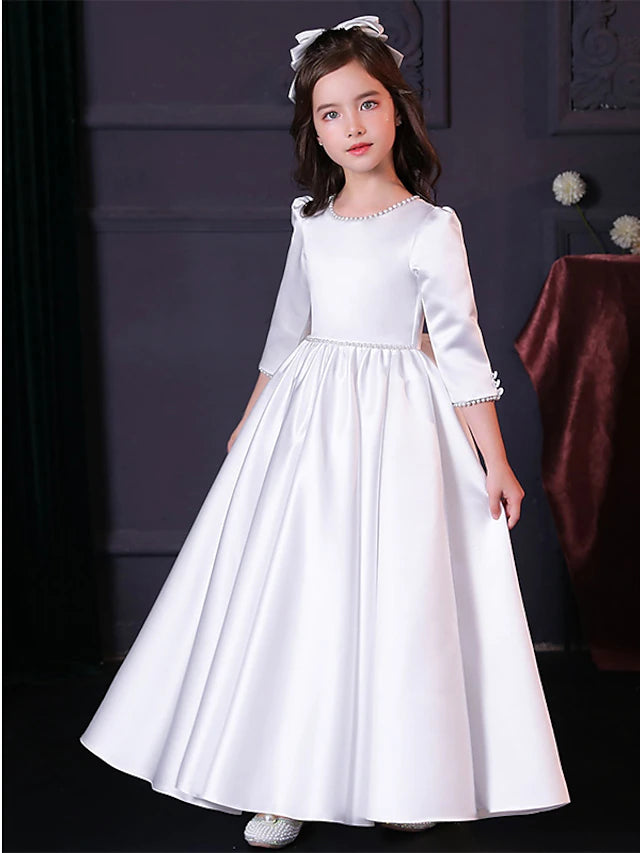 Girl wearing an elegant A-line floor length satin flower girl dress with faux pearl details.