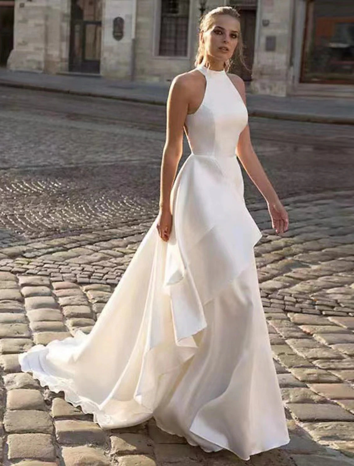 Model wearing an elegant white A-line halter wedding dress with an open back and flowing court train.