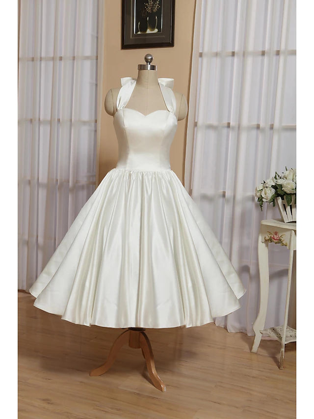 Front view of a white satin A-line tea-length dress with a halter neckline and bow detail.