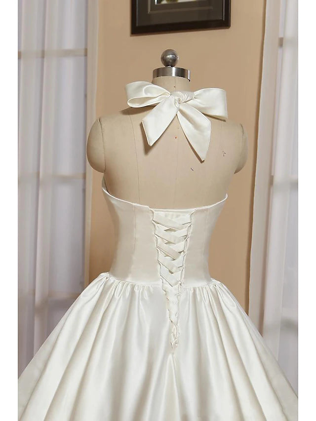 Side view of a white satin A-line tea-length dress with a halter neckline and pleats.