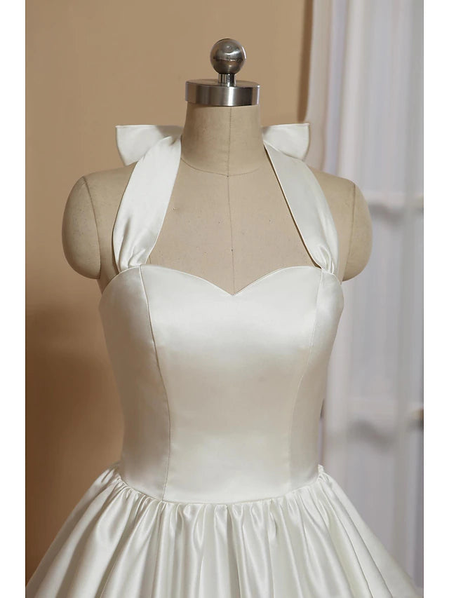 Back view of a white satin A-line tea-length dress, showing the halter neck and bow.