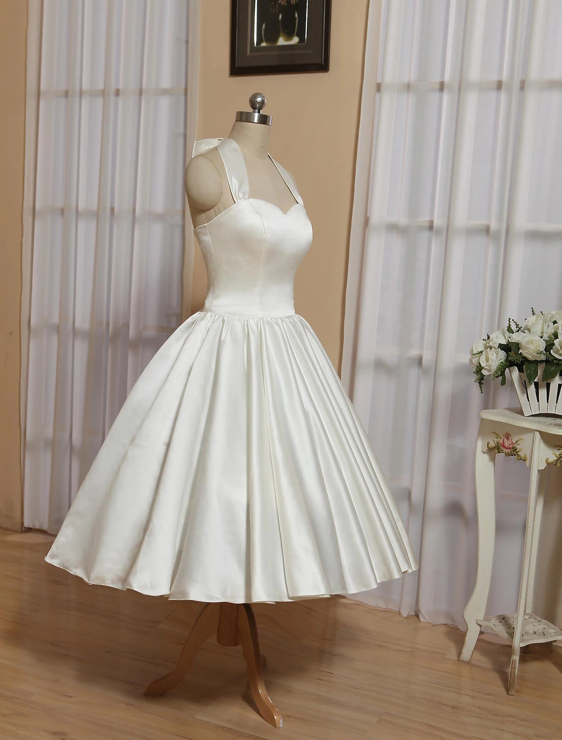 Model posing in white A-line halter tea length satin wedding dress.