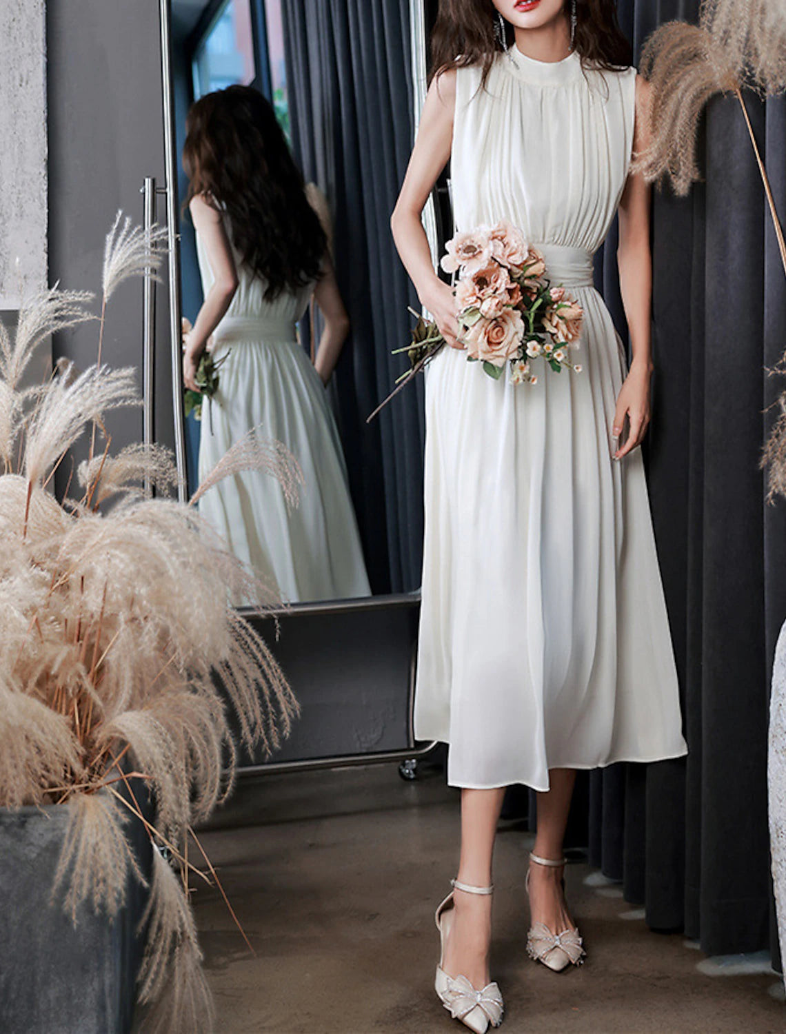 Side view of a white A-line high neck sleeveless tea length chiffon dress with pleats.
