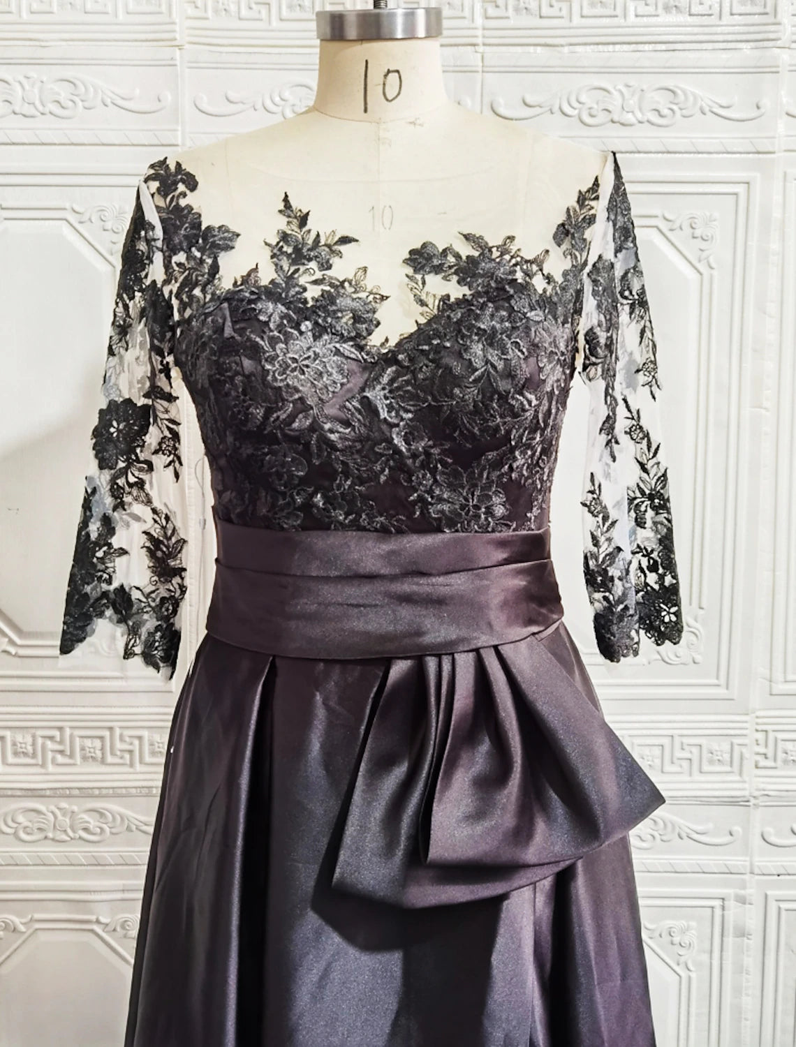 Woman wearing an elegant A-line satin formal gown with an illusion neckline and half sleeves.