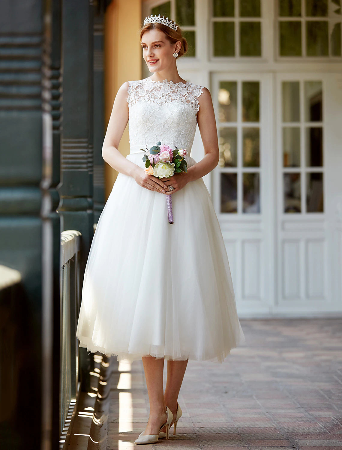 Model wearing a white A-line tea length lace wedding reception dress with illusion neckline, sash, and buttons.