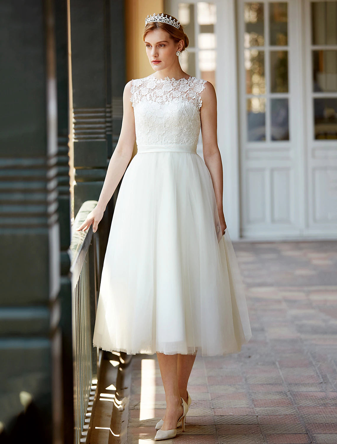 Side view of a white A-line tea length lace wedding reception dress with illusion neckline and sash.