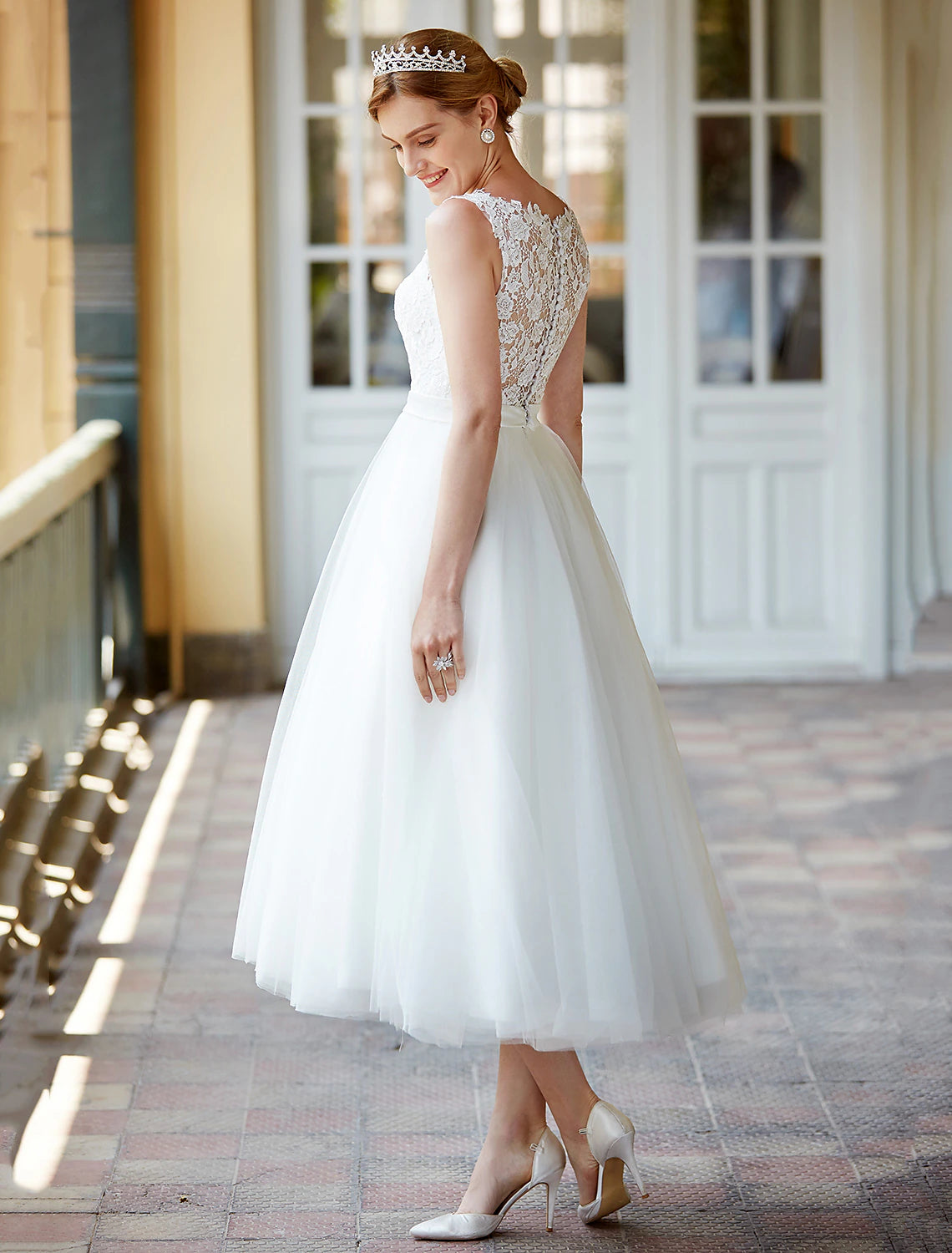 Model posing in a white A-line tea length lace wedding reception dress.