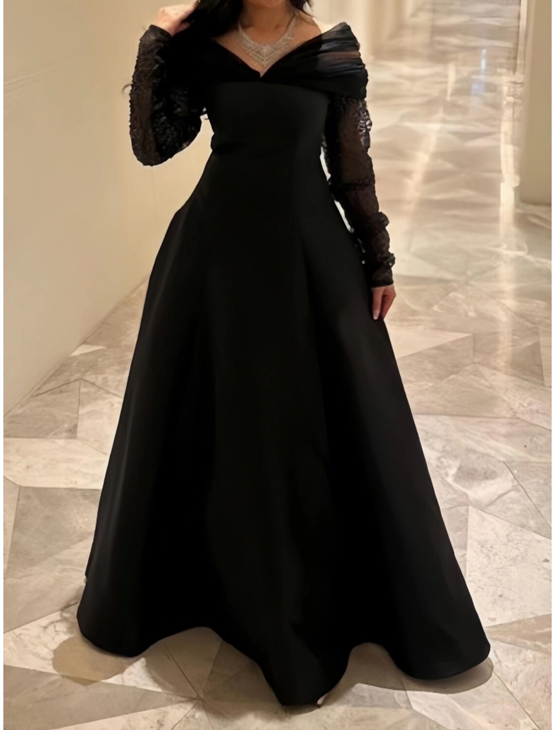 Close-up of the black satin fabric with sequin embellishments and pleats on the evening gown.