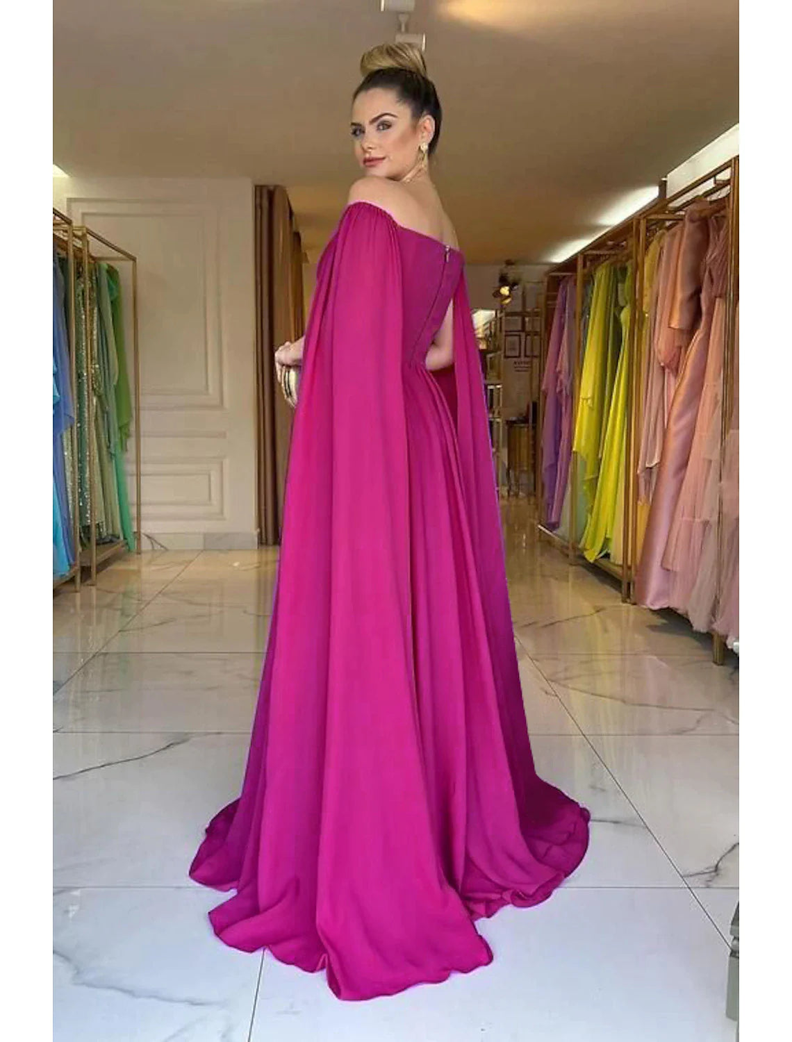 Woman posing in a flowing A-line off-shoulder gown, showing the back detail.