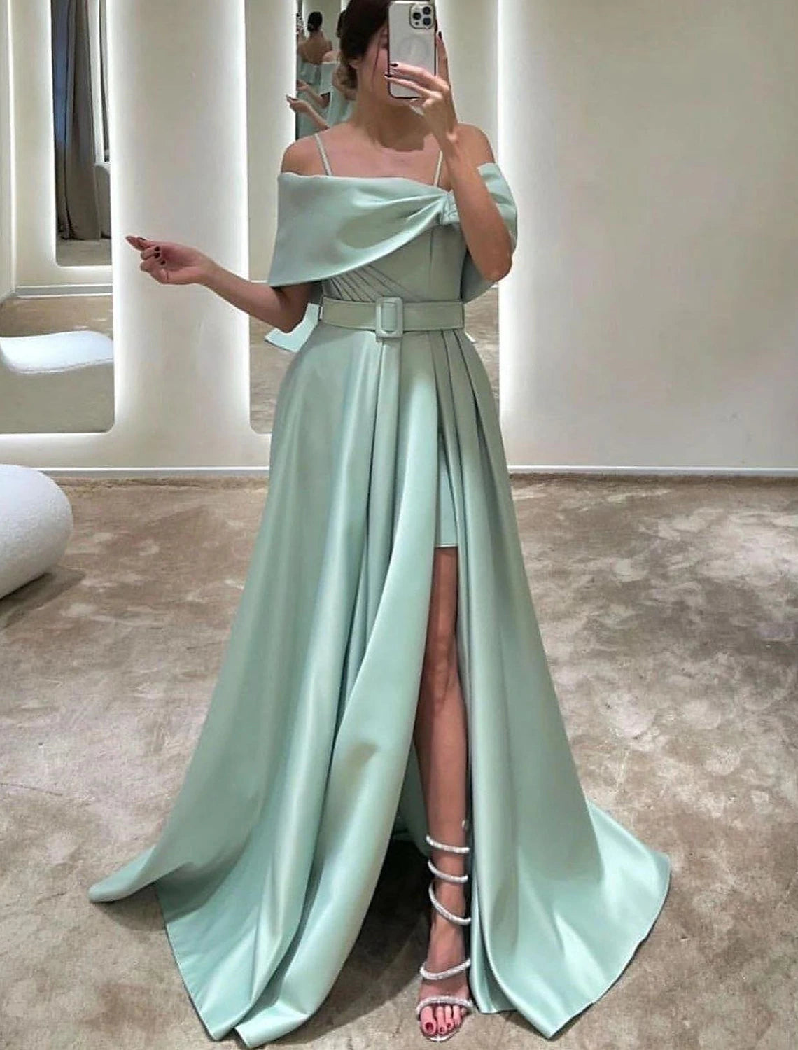 Model wearing an elegant A-line off-shoulder satin evening gown with crystal details and a front slit.