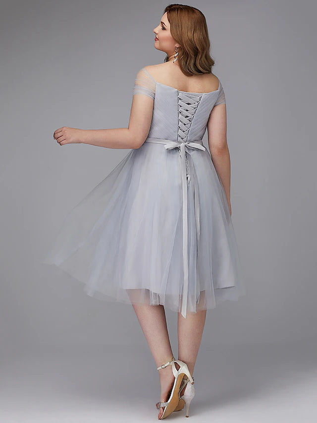 Model showcasing the back detail of an A-line off-shoulder tea length tulle dress with a criss-cross sash.