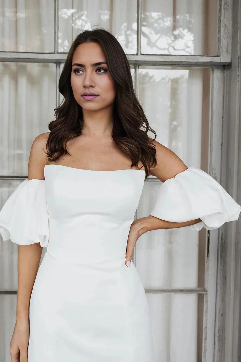 Side view of a woman in a short satin off-shoulder wedding dress.