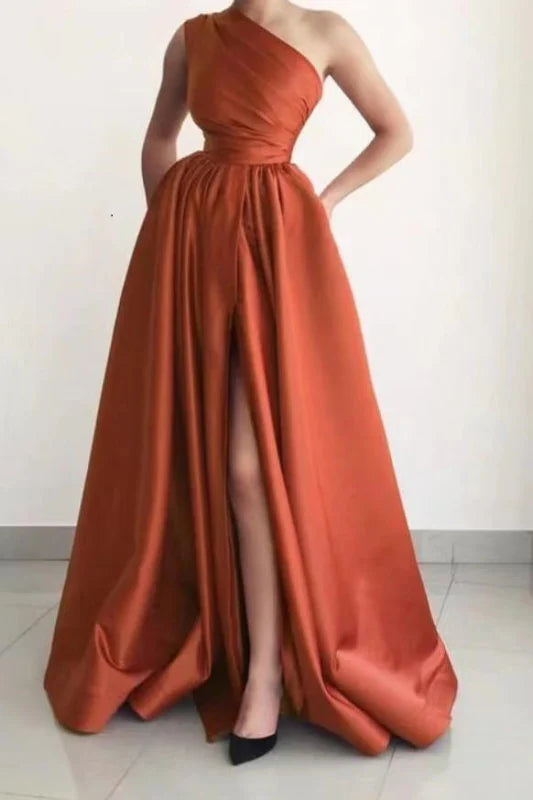 Woman wearing a navy A-line one-shoulder prom dress with a side split and pockets.