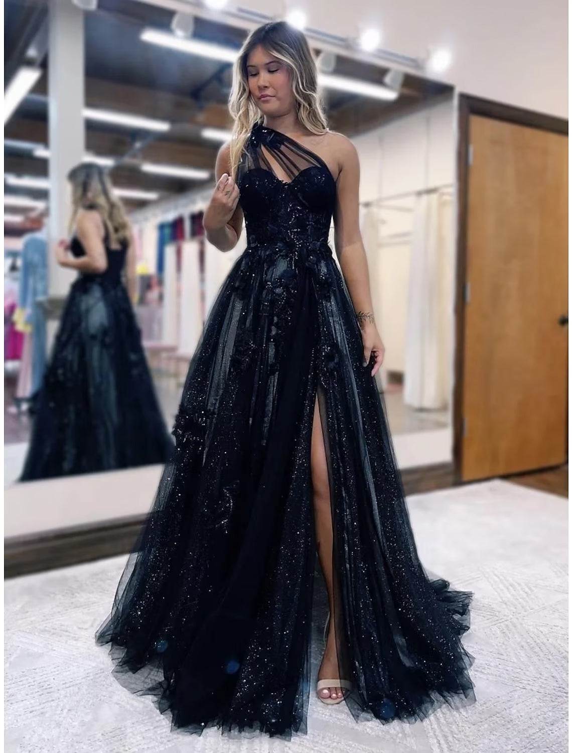 Full view of a model posing in a one-shoulder A-line prom dress with intricate appliques.