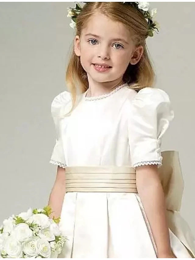Side profile of a girl wearing a white A-line satin flower girl dress.
