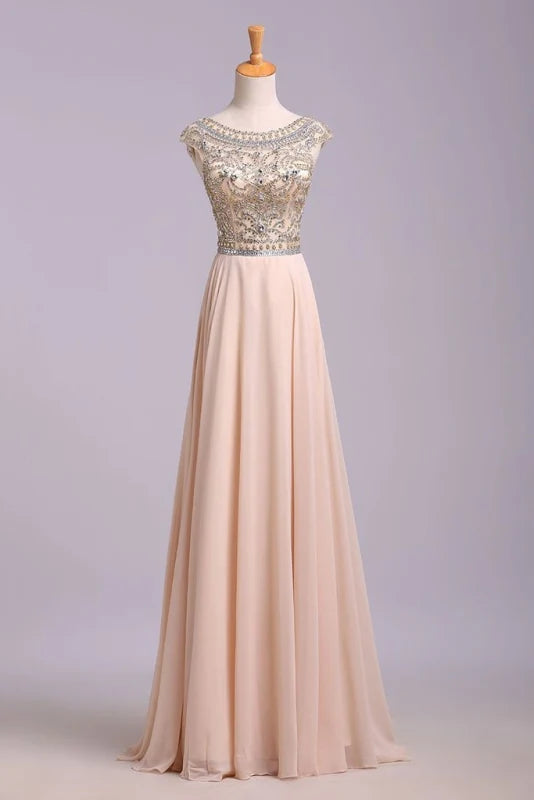 Model wearing an elegant A-line floor length prom dress with a scoop neck and beading.