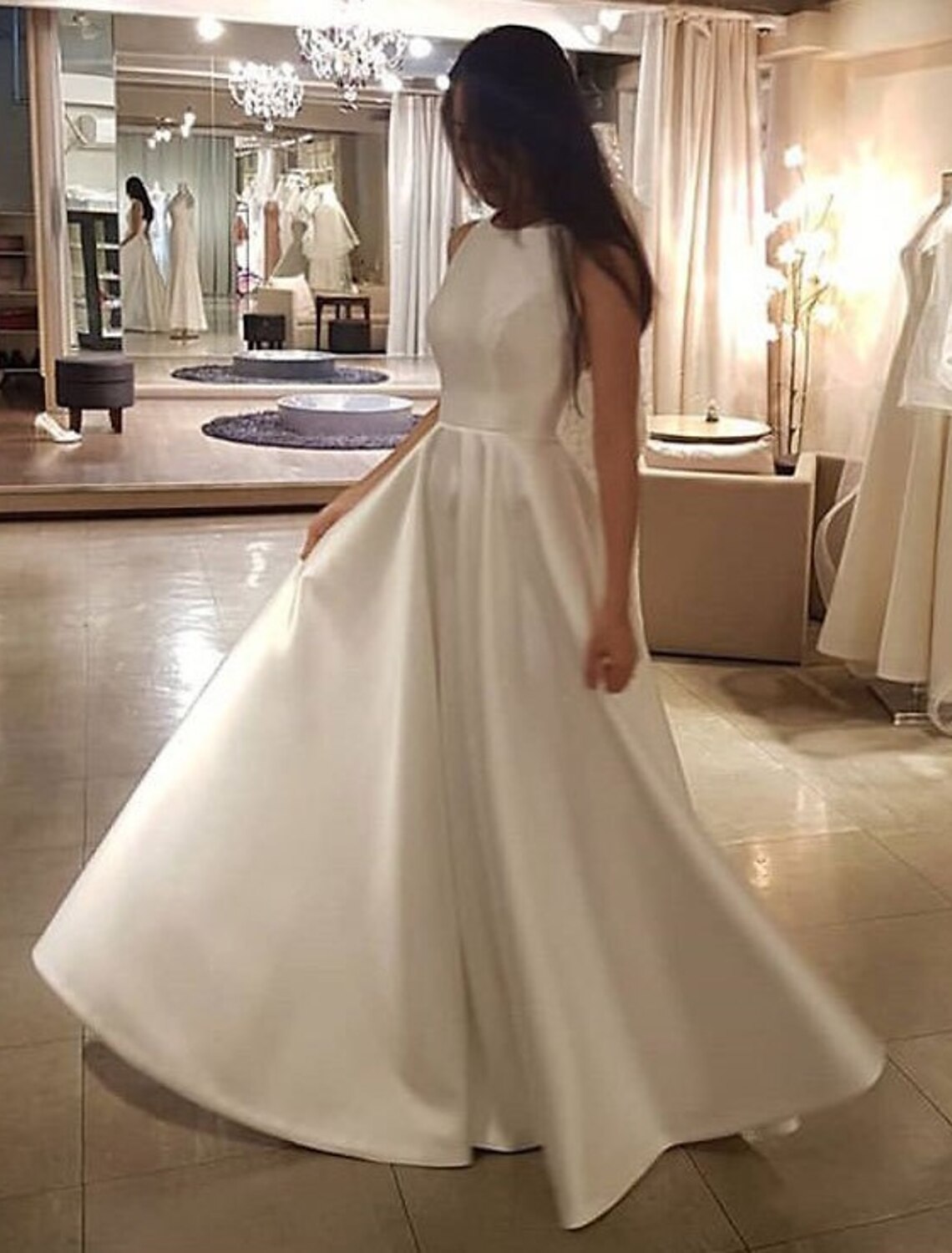 Woman wearing an elegant A-line white satin wedding dress with a scoop neck and sweep train.