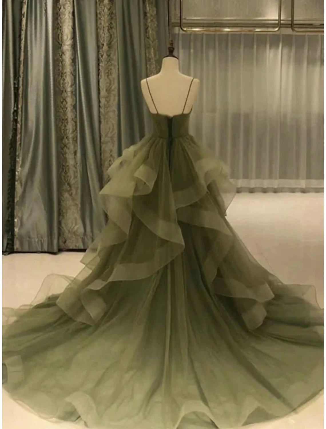 Model wearing an elegant green A-line prom dress with spaghetti straps, pleated tulle, ruffles, and a court train.