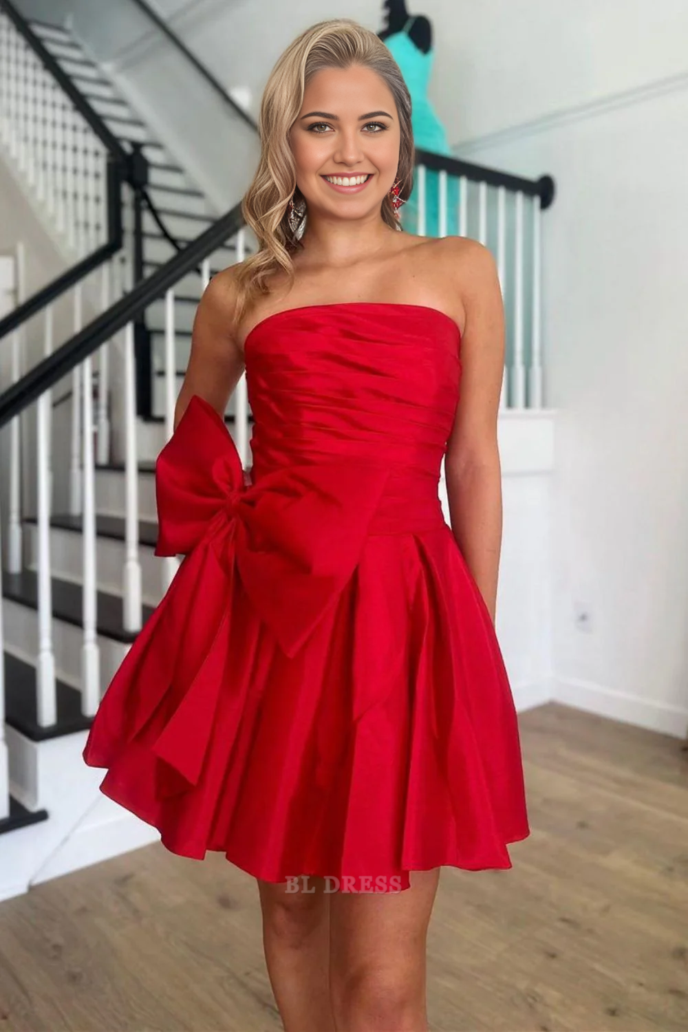 Model wearing a red strapless A-line short satin homecoming dress with a large bow on the back.