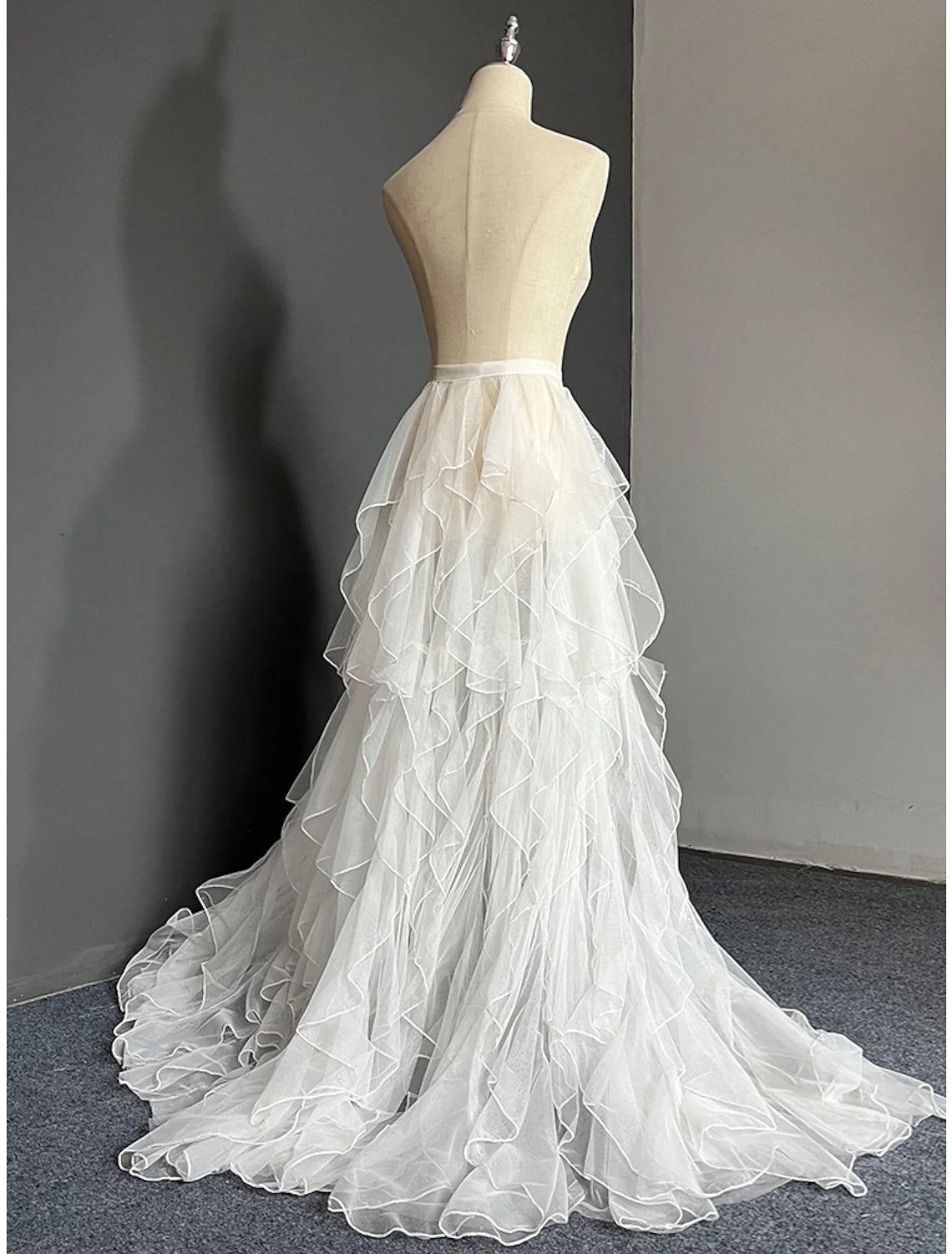 Side profile of a bride in a white A-line wedding dress with a dramatic court train tulle overskirt.