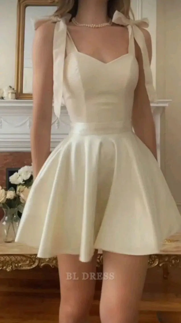 Ivory satin mini homecoming dress with bow shoulder straps and pleated skirt.