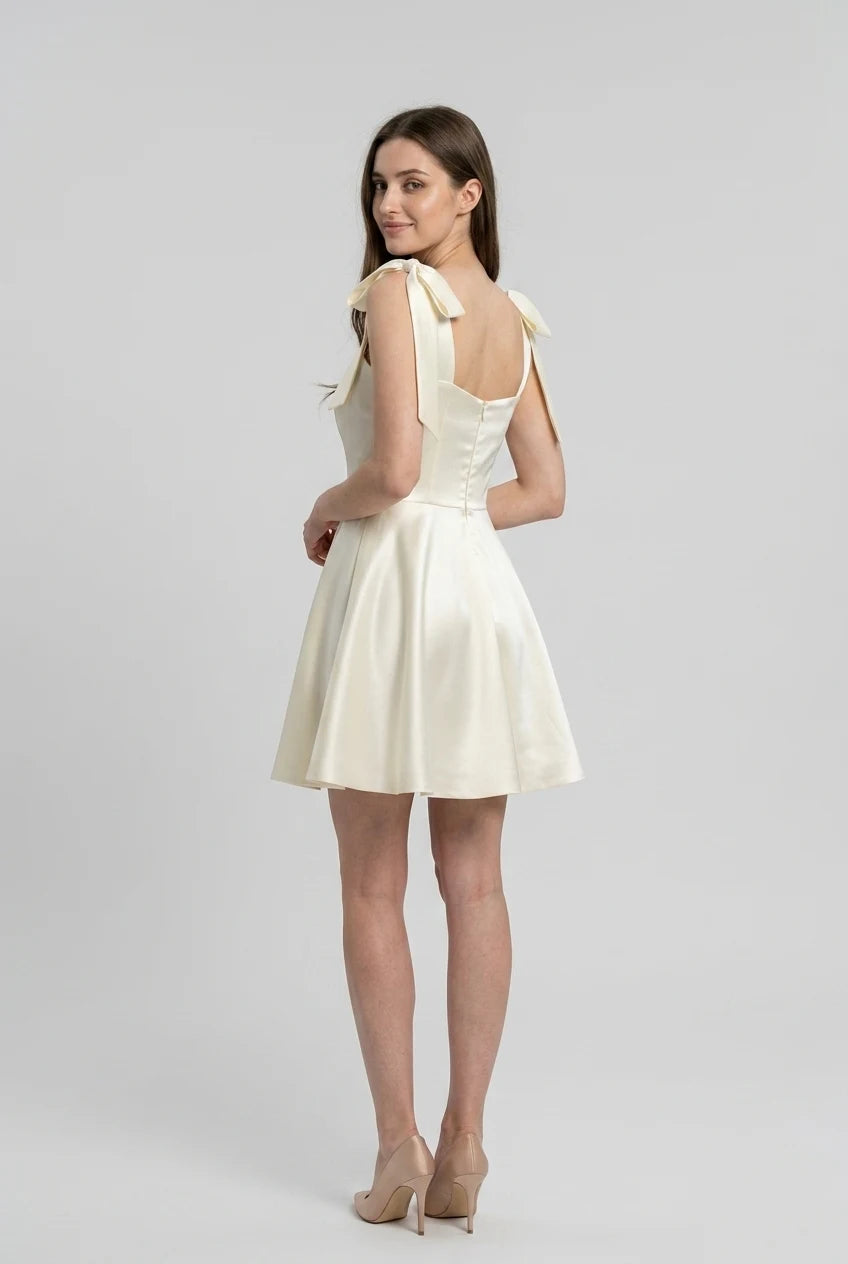 Model wearing an ivory satin mini dress, showing the A-line pleated skirt.
