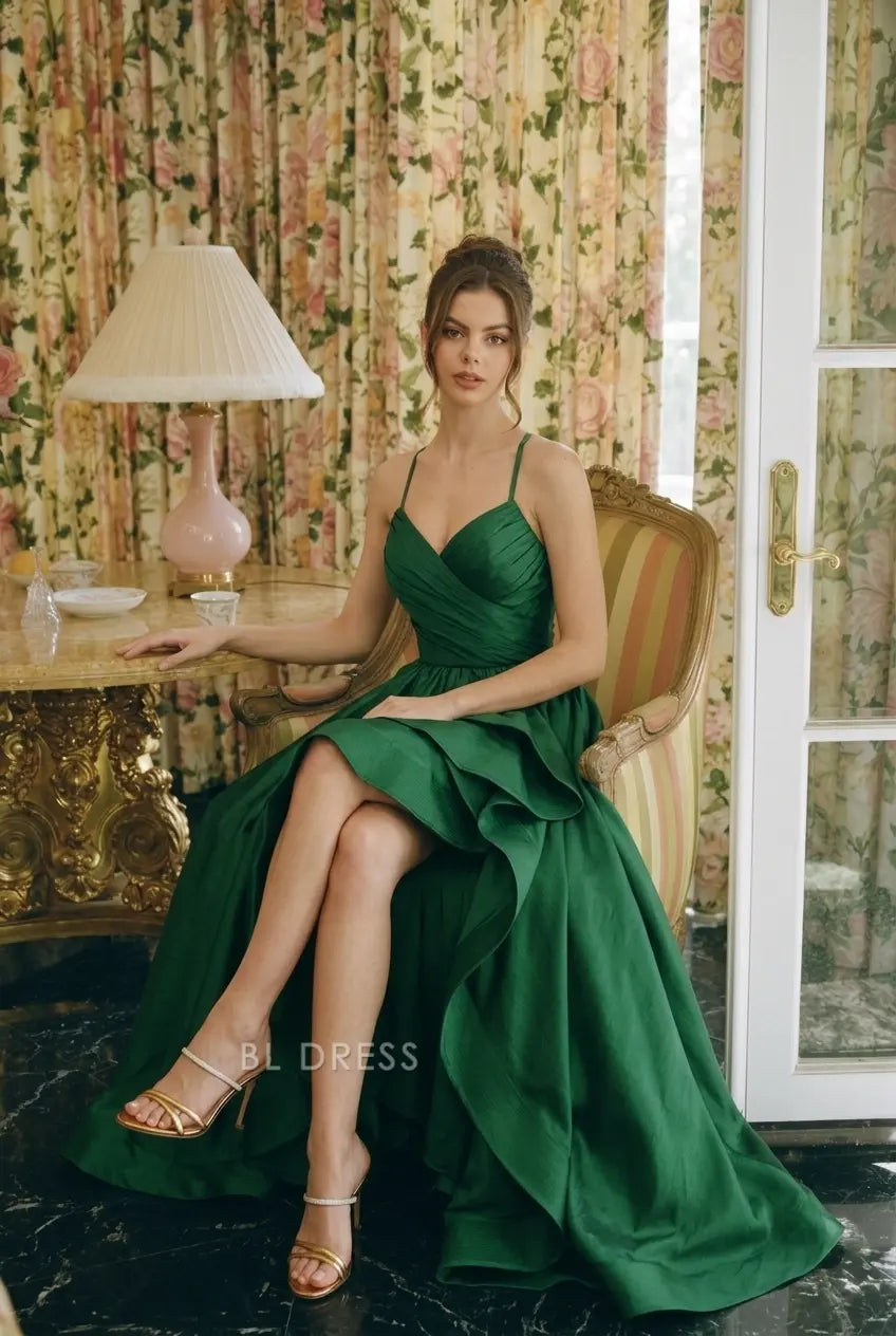 Model posing in emerald green A-line gown, showcasing high slit and flowing ruffles.