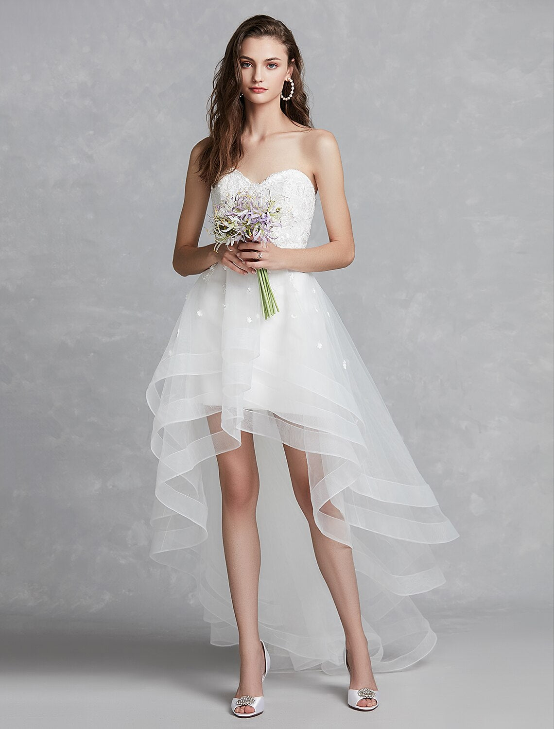 Elegant A-line sweetheart strapless white bridal gown with lace appliques and asymmetrical hem.