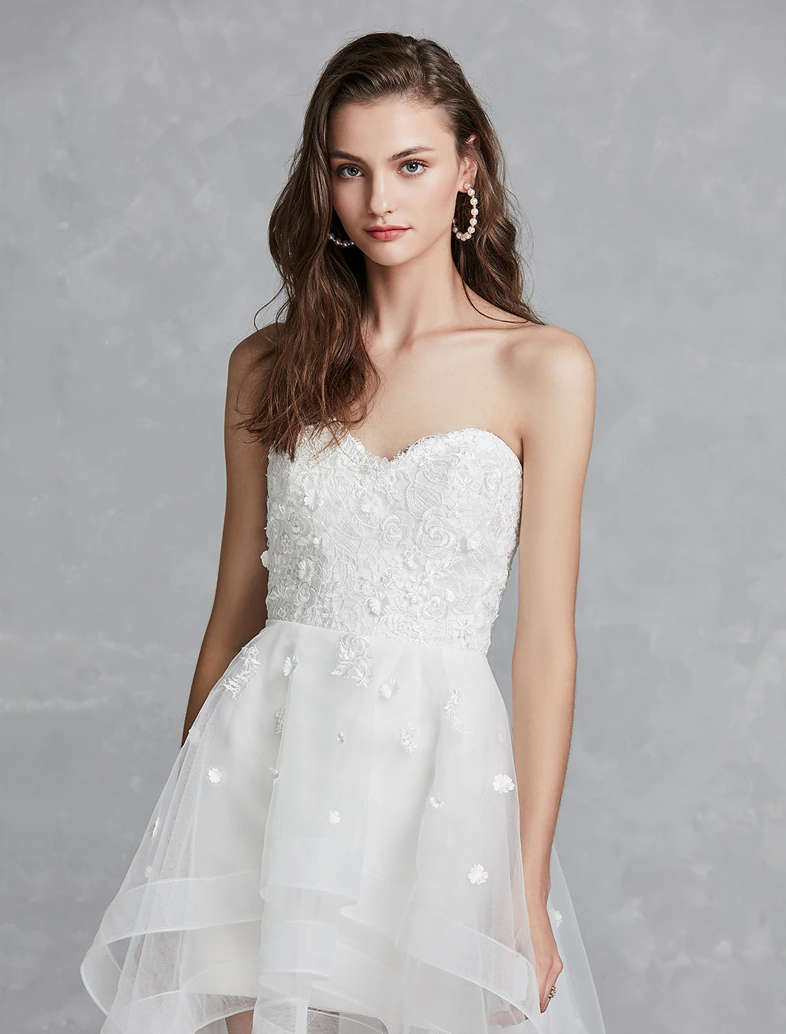 Elegant A-line sweetheart strapless white bridal gown with lace appliques and asymmetrical hem.