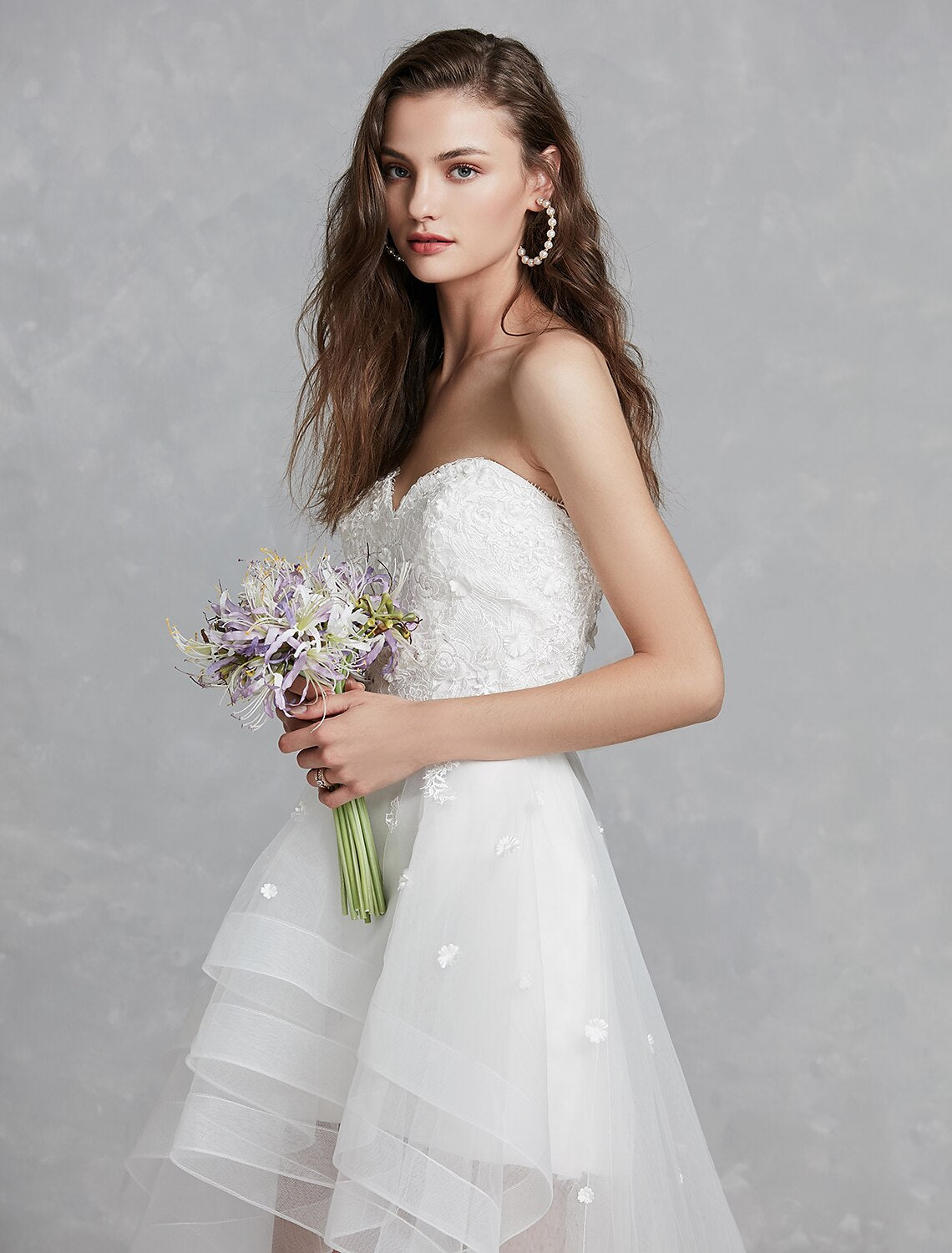 Elegant A-line sweetheart strapless white bridal gown with lace appliques and asymmetrical hem.