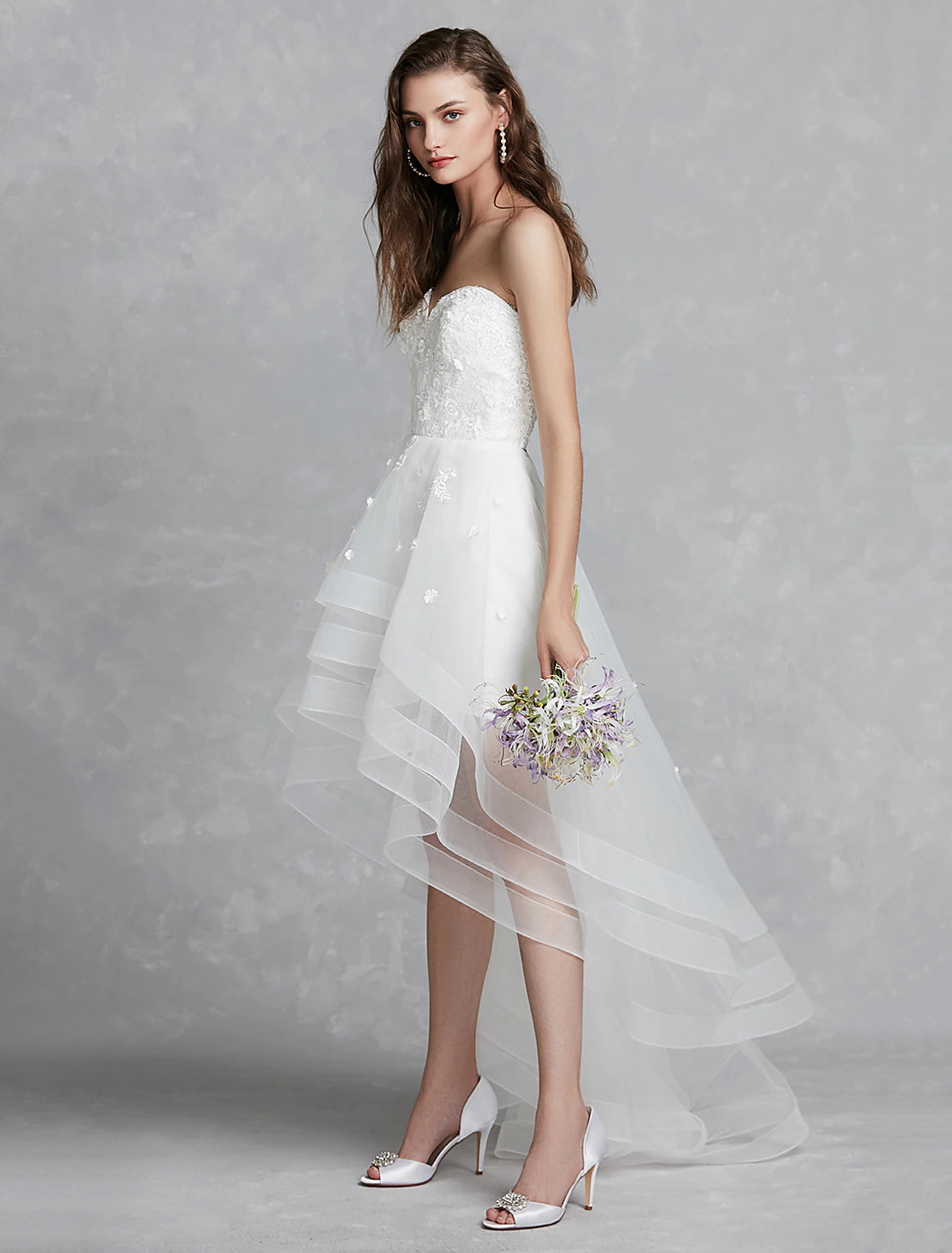 Elegant A-line sweetheart strapless white bridal gown with lace appliques and asymmetrical hem.