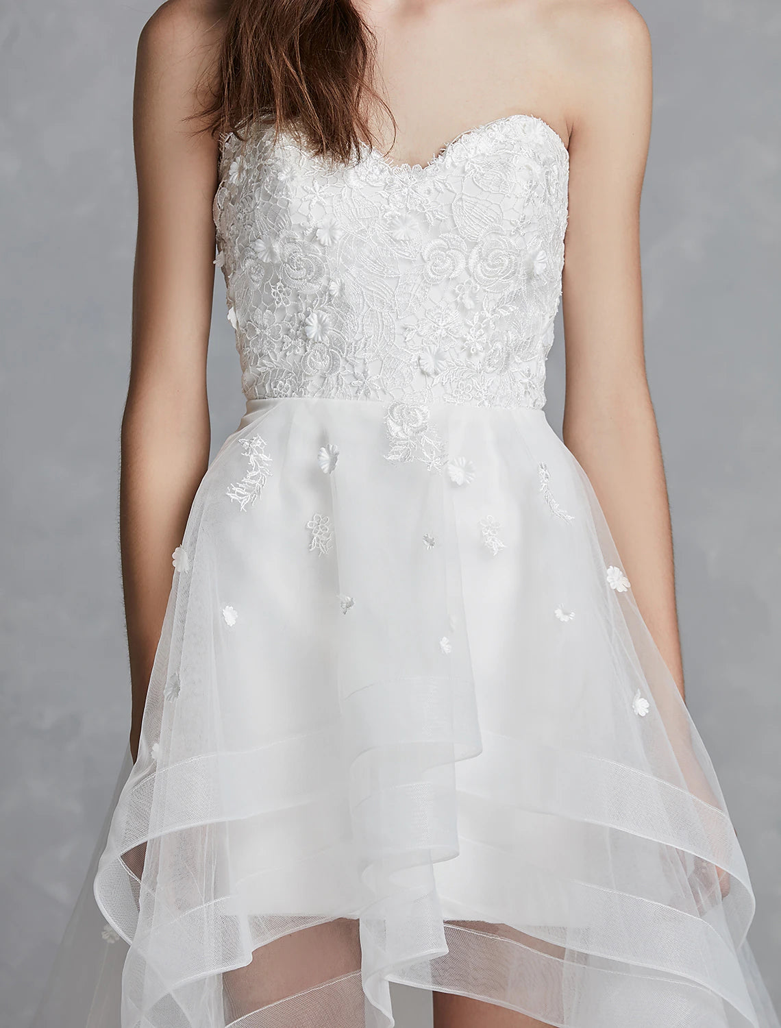 Elegant A-line sweetheart strapless white bridal gown with lace appliques and asymmetrical hem.
