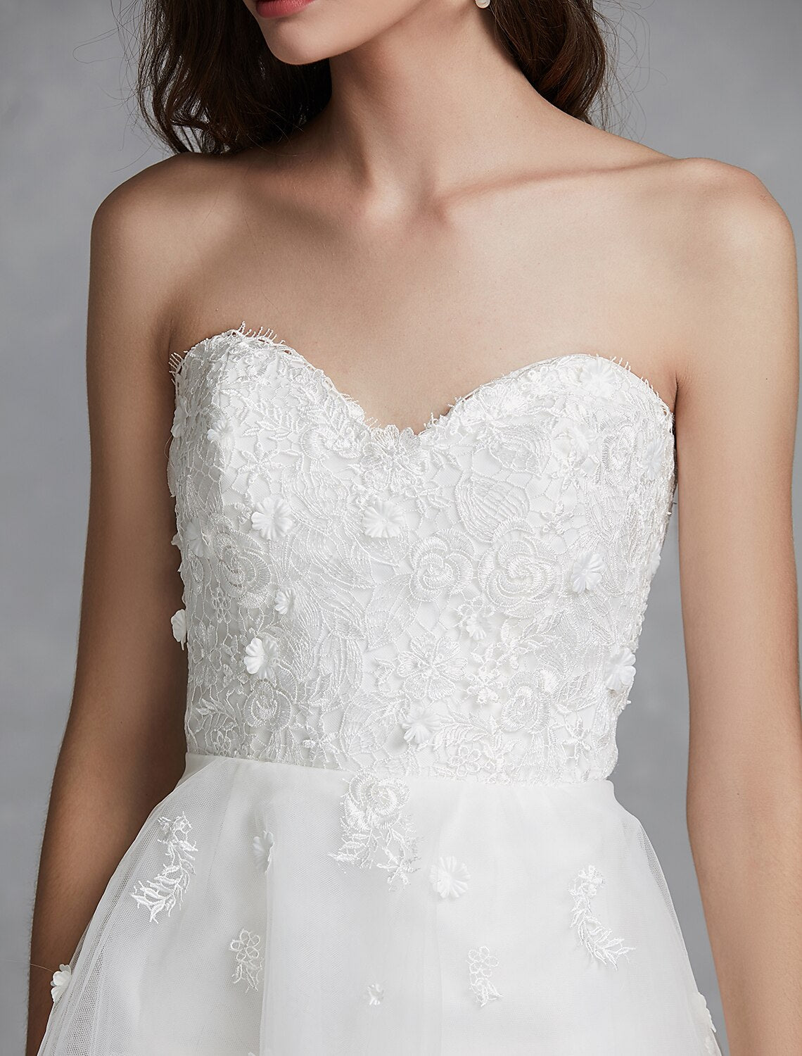 Elegant A-line sweetheart strapless white bridal gown with lace appliques and asymmetrical hem.